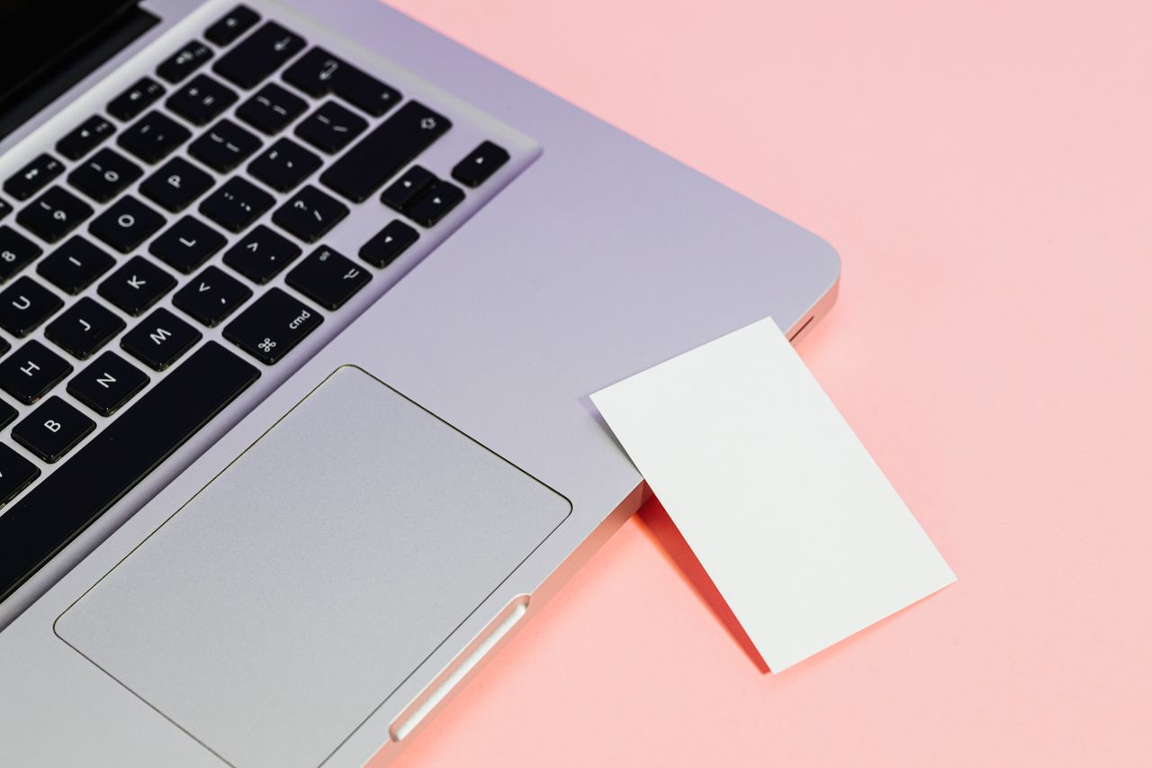 Close-up of a laptop with a blank card on a pink background, ideal for tech concepts.
