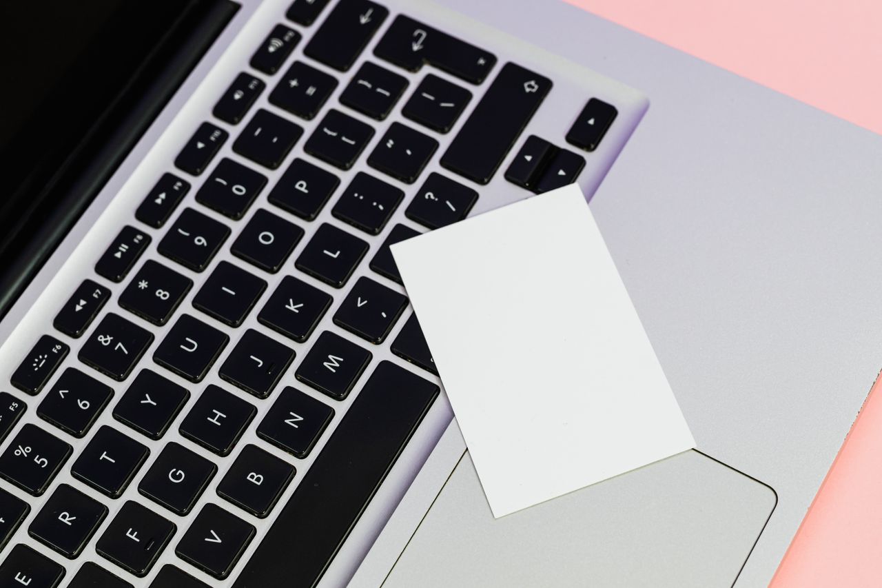 Modern flat lay of a laptop keyboard with a blank white card on a pink surface. Perfect for technology themes.