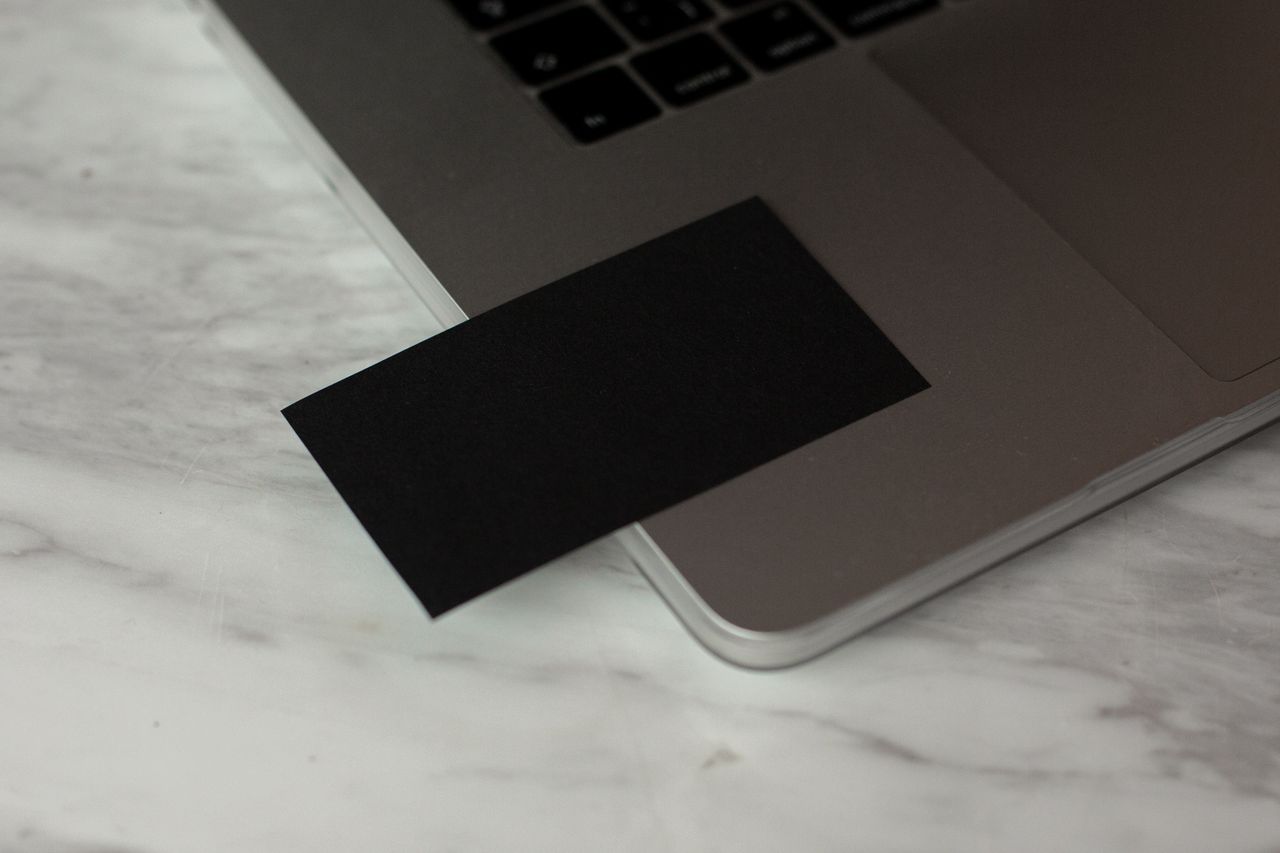 From above of black mock up business card placed on opened modern gray laptop on marble table in contemporary workplace